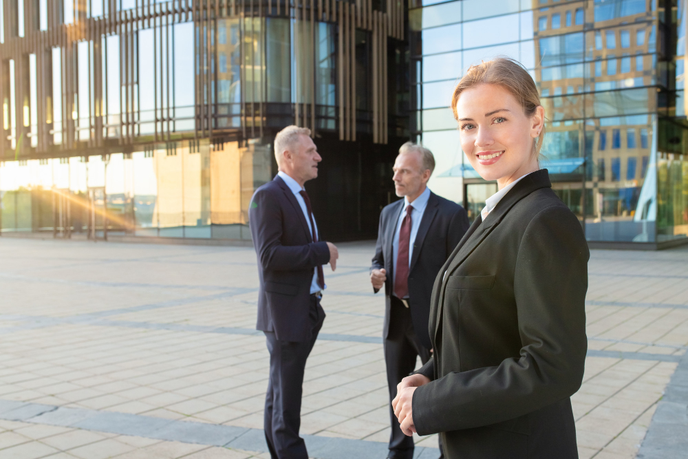 Confident young businesswoman in office suit talking on mobile phone and gesturing outdoors. businesspeople and city building glass facade in background. copy space. business communication concept